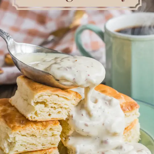 A photo of a plate of golden, flaky biscuits layered with buttery folds and a generous ladle of creamy sausage gravy, speckled with bits of browned sausage and flecks of freshly cracked black pepper. The gravy glistens under warm lighting. In the background, a rustic wooden table is adorned with a soft gingham napkin and a steaming cup of coffee, creating a cozy, homestyle vibe. The title text overlay "Pioneer Woman Southern Biscuits and Sausage Gravy" is done in a soft feminine country font.